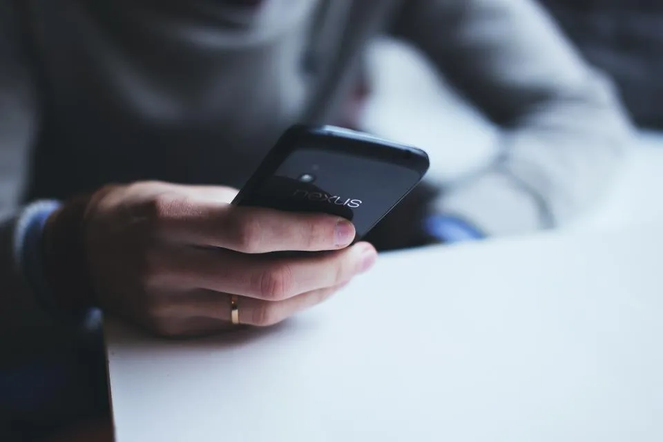 A hand holding a smartphone at a desk